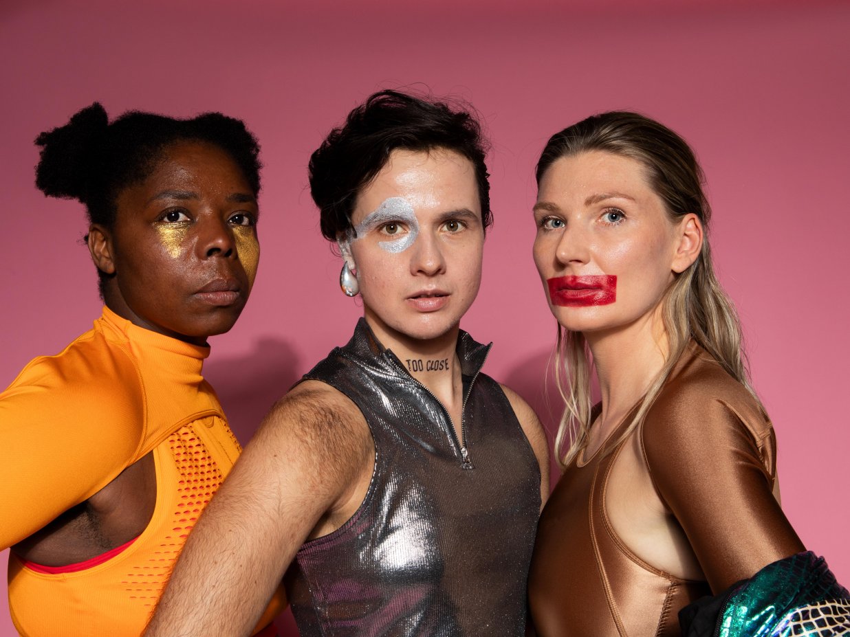 Wir sehen drei Personen, die k&auml;mpferisch und verschwitzt in die Kamera blicken.