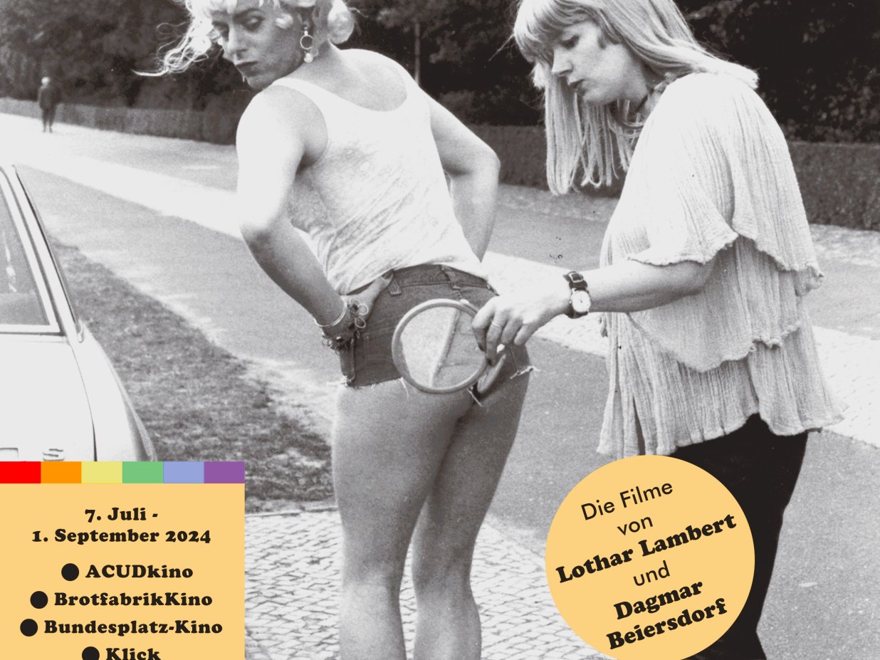 Auf der Stra&szlig;e stehend, hilft eine Frau einer aufreizend gekleideten Transfrau mittels eines Spiegels den Sitz ihrer sehr knappen Shorts zu &uuml;berpr&uuml;fen.