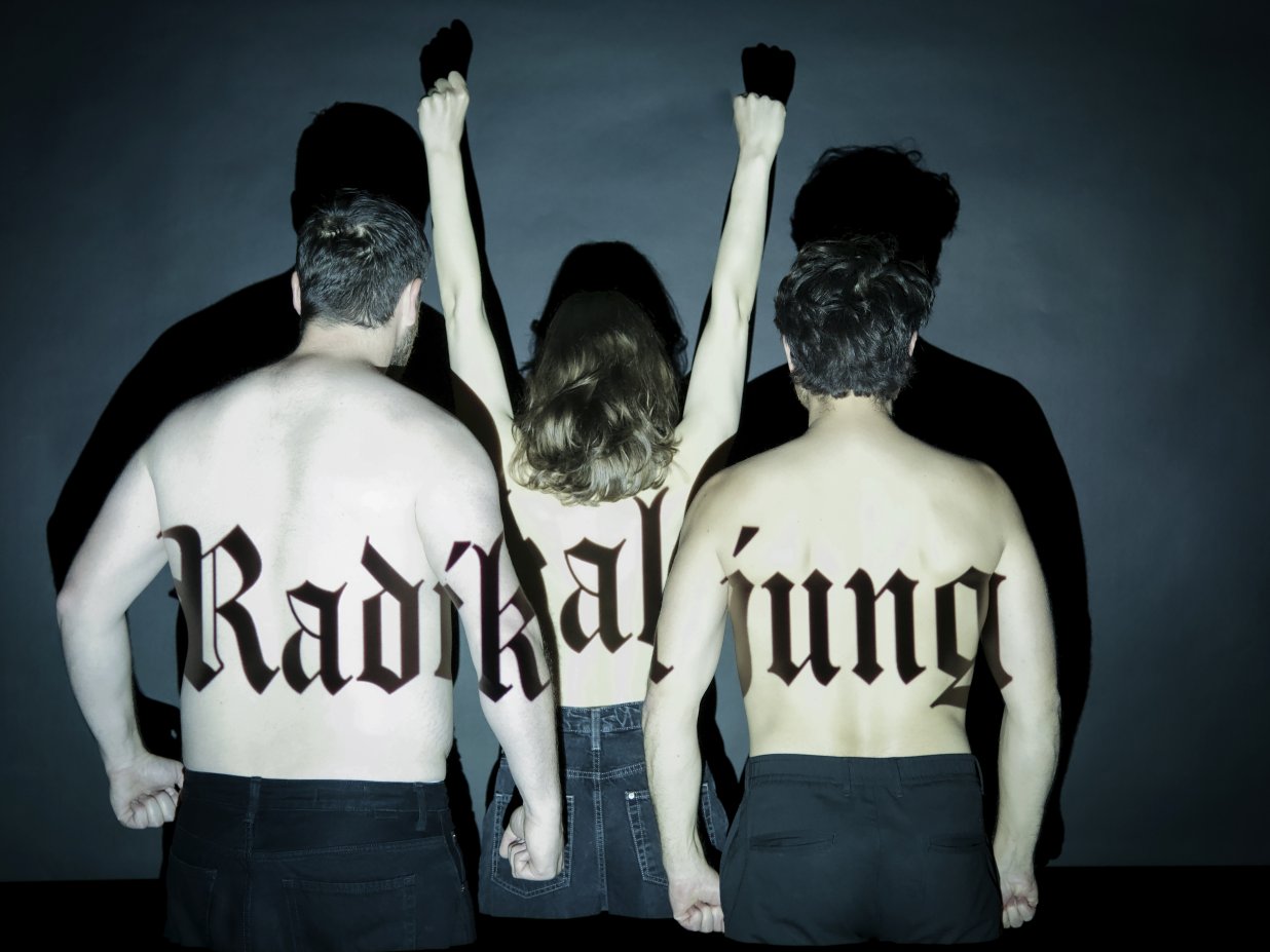 Drei Personen stehen mit nacktem R&uuml;cken zur Kamera, eine rei&szlig;t die Arme nach oben und auf ihrer Haut steht der Schriftzug "Radikal jung".