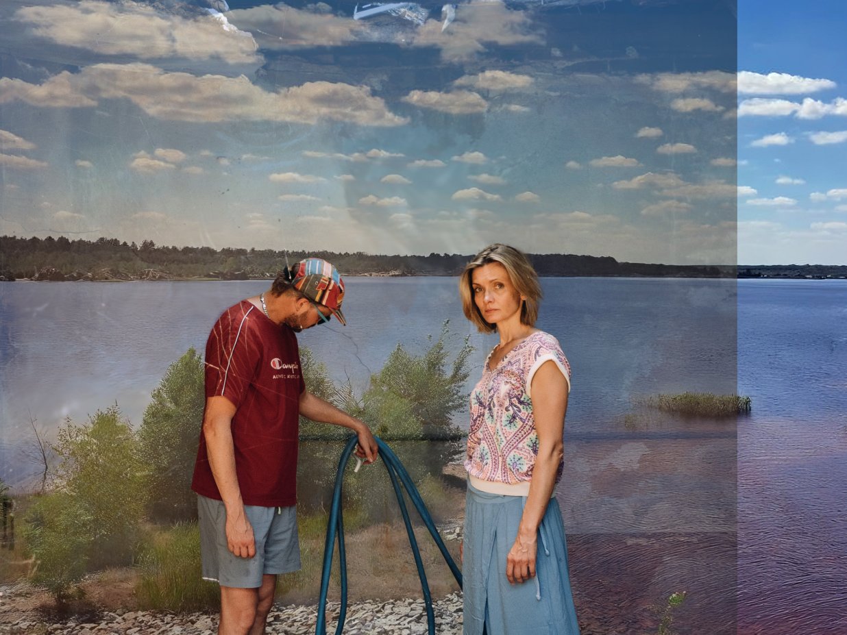 Zwei Personen, eine m&auml;nnlich und eine weiblich gelesene stehen an einem Kiesstrand, im Hintergrund der See und Himmel. Die Frau blickt kritisch in die Kamera, der Mann hat sein Gesicht abgew